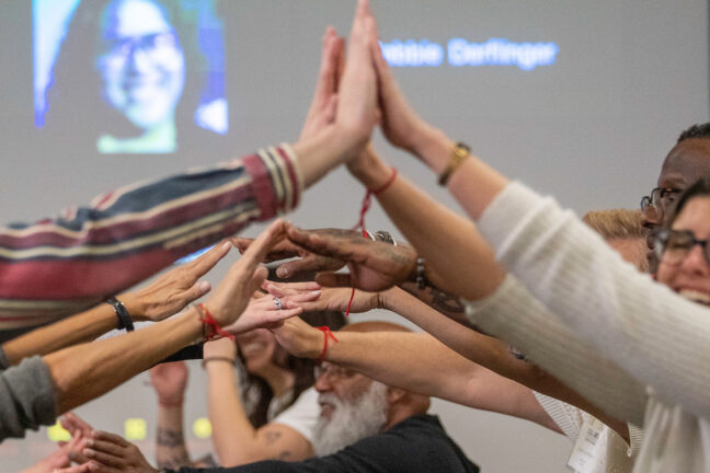 View of many different people's arms and hands coming together from opposite directions. A few smiling faces are visible.