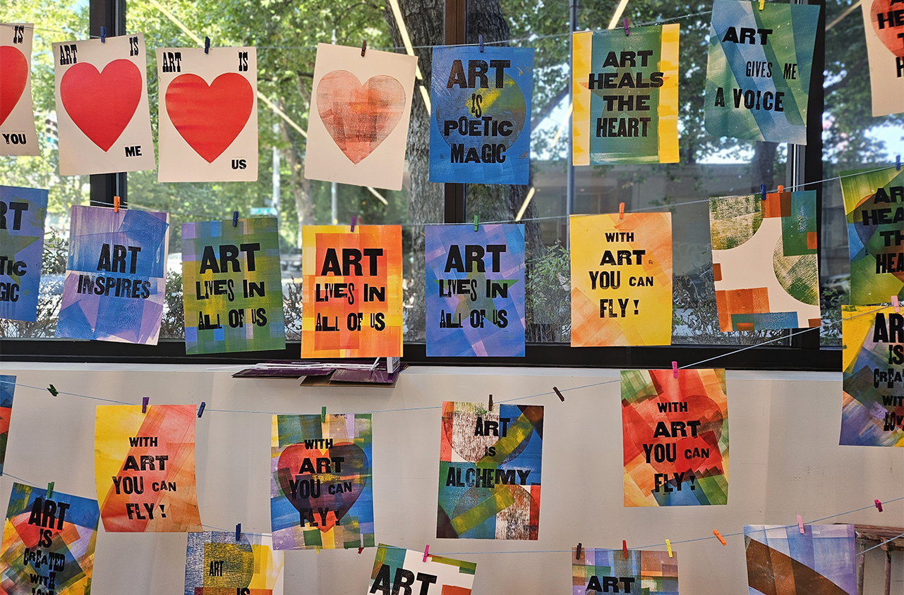 Colorful prints hanging on a clothesline with phrases like "Art lives in all of us" and "Art heals the heart."