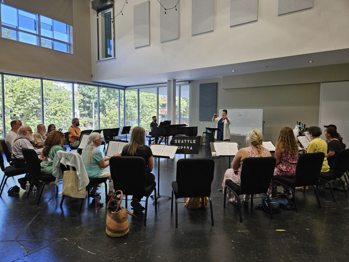 A choir group reherses in a large room with vaulted ceilings and picture windows.